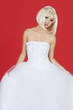 Photo: Portrait of beautiful young woman in wedding dress standing against red background Portrait of beautiful young woman in wedding dress standing against red background