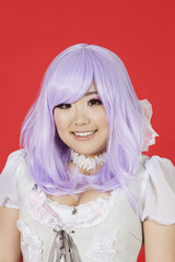 Photo: Portrait of cute young woman in doll costume and purple wig over red background Portrait of cute young woman in doll costume and purple wig over red background