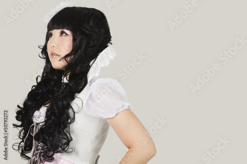 Photo: Side view of thoughtful young woman in doll costume looking away against gray background Side view of thoughtful young woman in doll costume looking away against gray background