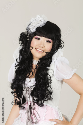Photo: Portrait of cute happy young woman in doll costume posing over gray background Portrait of cute happy young woman in doll costume posing over gray background