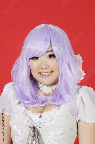 Photo: Portrait of cute young woman in doll costume and purple wig over red background Portrait of cute young woman in doll costume and purple wig over red background
