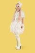 Photo: Full length portrait of young woman dressed as a doll over yellow background Full length portrait of young woman dressed as a doll over yellow background