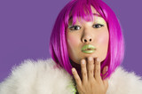 Photo: Portrait of young funky woman in pink wig blowing kiss over purple background Portrait of young funky woman in pink wig blowing kiss over purple background