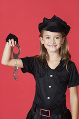 Photo: Portrait of young girl in police costume holding handcuffs against red background Portrait of young girl in police costume holding handcuffs against red background
