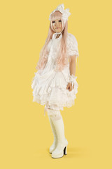 Photo: Full length portrait of young woman dressed as a doll over yellow background Full length portrait of young woman dressed as a doll over yellow background