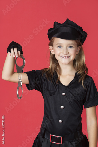 Photo: Portrait of young girl in police costume holding handcuffs against red background Portrait of young girl in police costume holding handcuffs against red background
