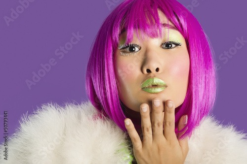 Photo: Portrait of young funky woman in pink wig blowing kiss over purple background Portrait of young funky woman in pink wig blowing kiss over purple background