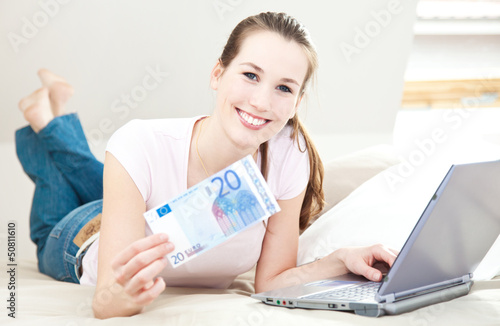 Photo: Attraktive junge Frau mit Laptop hält 20 Euro Attraktive junge Frau mit Laptop hält 20 Euro