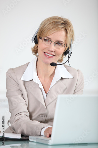 Photo: Woman using a telephone headset at a laptop computer Woman using a telephone headset at a laptop computer