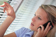 Woman on the phone looking through venetian blinds