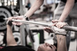 Photo: Young man lifting the barbell in the gym with instructor. Young man lifting the barbell in the gym with instructor.