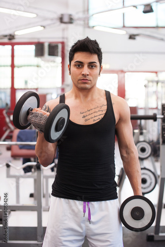 Photo: Young man exercising with dumbbells in a gym. Young man exercising with dumbbells in a gym.