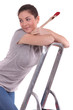 Woman holding paint brush whilst climbing ladder