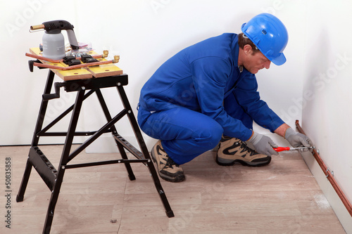Photo: Plumber fitting copper pipes to a wall Plumber fitting copper pipes to a wall