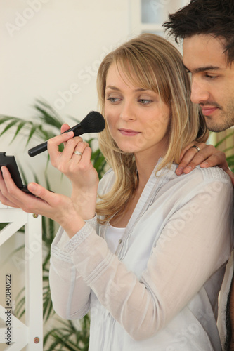 Photo: Woman applying blusher whilst boyfriend watches Woman applying blusher whilst boyfriend watches