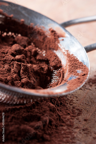 Photo: Cocoa powder on colander over wooden table Cocoa powder on colander over wooden table