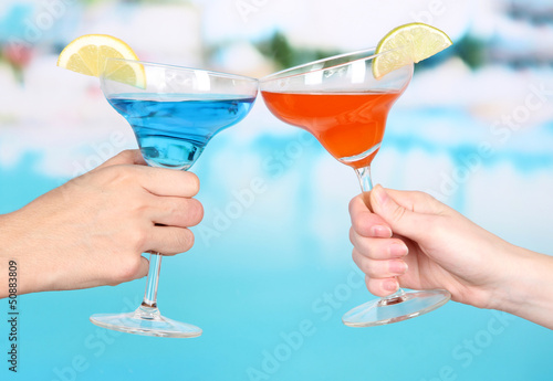 Photo: Cocktails in men's and women's hands on pool background Cocktails in men's and women's hands on pool background