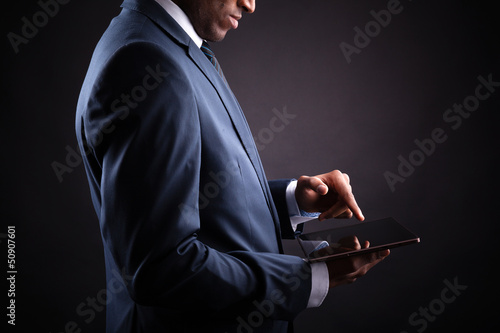 Photo: Businessman working on a digital tablet against black backgroun Businessman working on a digital tablet against black backgroun