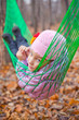 A girl lies in green hammock in the autumn forest