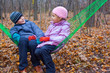 Brother and sister sitting together in hammock in autumn forest