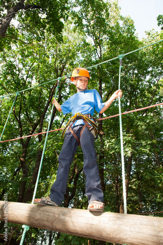 Photo: Young guy with equipment climber moves on balk holding ropes. Young guy with equipment climber moves on balk holding ropes.