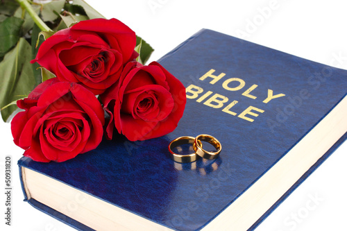Photo: Wedding rings with roses on bible isolated on white Wedding rings with roses on bible isolated on white