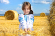 small rural girl on harvest field with straw bales