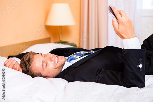 Photo: Geschäftsmann liest SMS im Hotelbett Geschäftsmann liest SMS im Hotelbett