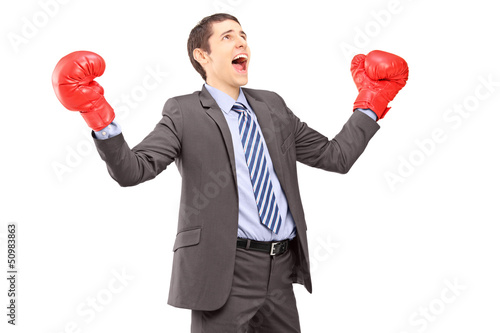 Photo: Happy young businessman in suit with red boxing gloves gesturing Happy young businessman in suit with red boxing gloves gesturing