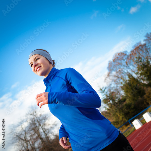 Photo: Young woman running at a track and field stadium Young woman running at a track and field stadium