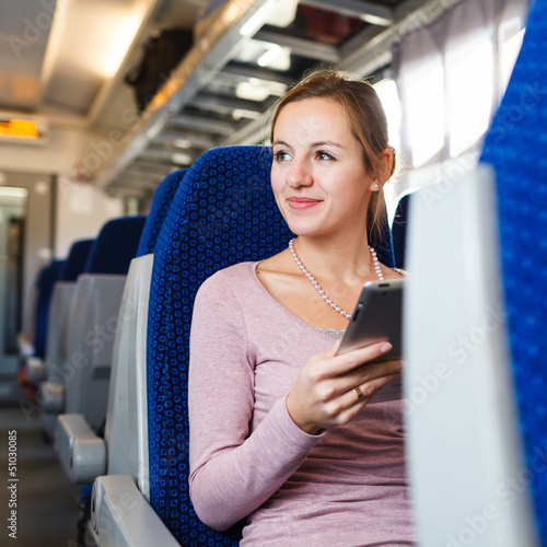 Photo: Young woman using her tablet computer while traveling by train Young woman using her tablet computer while traveling by train