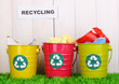 Recycling bins on green grass near wooden fence