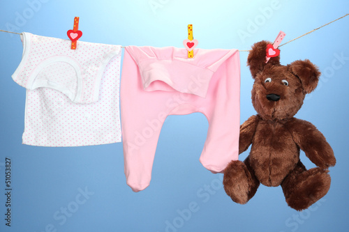Photo: Baby clothes hanging on clothesline, on color background Baby clothes hanging on clothesline, on color background