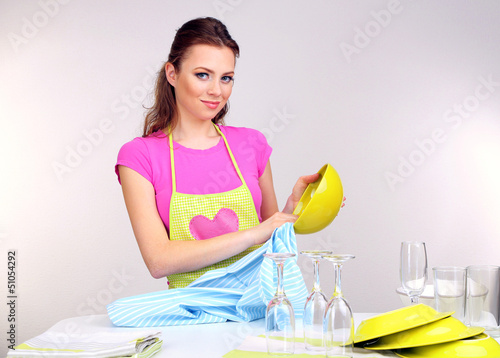 Photo: Beautiful young woman wipes clean utensils in kitchen Beautiful young woman wipes clean utensils in kitchen
