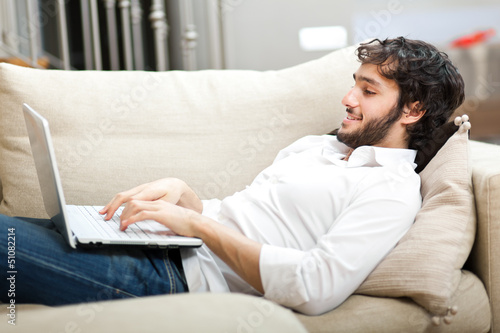 Photo: Portrait of a relaxed young guy using laptop at home Portrait of a relaxed young guy using laptop at home