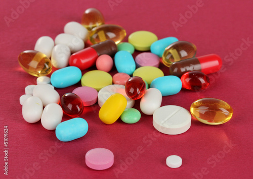 Photo: Assortment of pills, tablets and capsules on red background Assortment of pills, tablets and capsules on red background