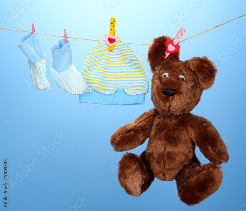 Photo: Baby clothes hanging on clothesline, on blue background Baby clothes hanging on clothesline, on blue background