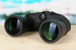 Black modern binoculars on wooden table on blue background
