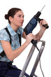 Woman holding drill whilst climbing ladder