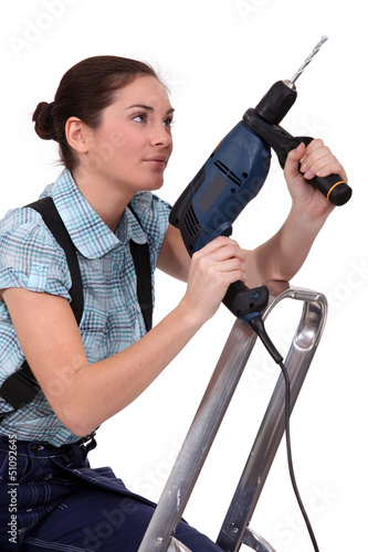 Photo: Woman holding drill whilst climbing ladder Woman holding drill whilst climbing ladder