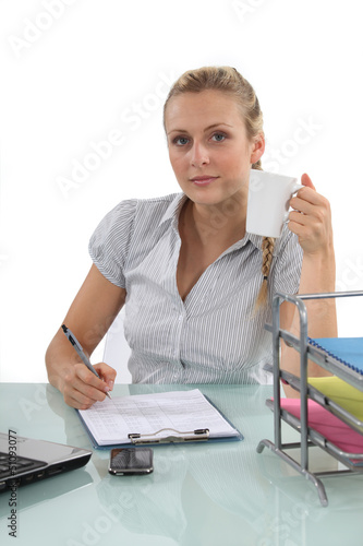 Photo: Young woman having a coffee at her desk Young woman having a coffee at her desk