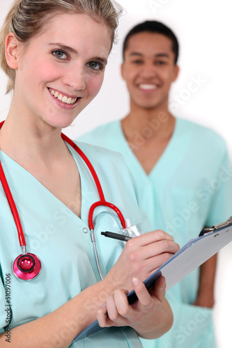 Photo: Nurse with clip-board stood with colleague Nurse with clip-board stood with colleague