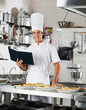 Chef With Book Standing By Kitchen Counter