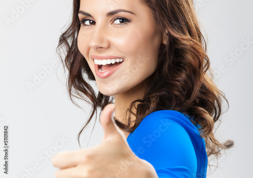 Photo: Young woman with thumbs up gesture, over grey Young woman with thumbs up gesture, over grey