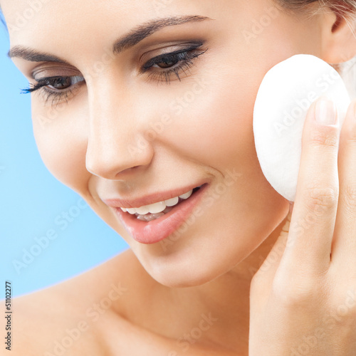 Photo: Young woman cleaning skin by cotton pad, over blue Young woman cleaning skin by cotton pad, over blue