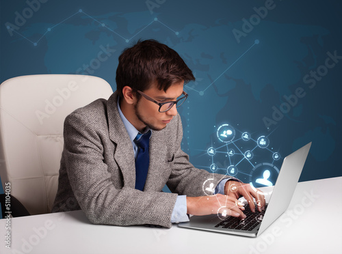Photo: Young man sitting at desk and typing on laptop with social netwo Young man sitting at desk and typing on laptop with social netwo