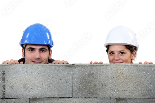 Photo: male bricklayer and female counterpart hiding behind wall male bricklayer and female counterpart hiding behind wall