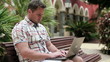 Young man with laptop sitting in the city, steadicam shot
