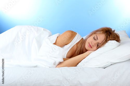 Photo: young beautiful woman sleeping on bed on blue background young beautiful woman sleeping on bed on blue background
