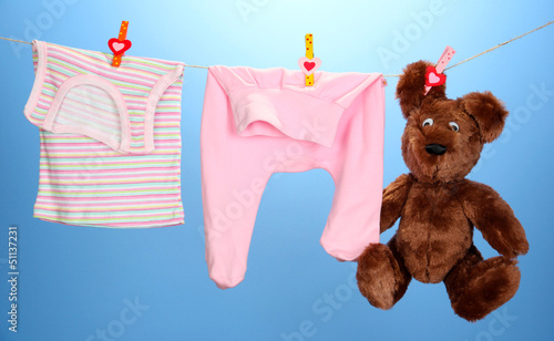 Photo: Baby clothes hanging on clothesline, on color background Baby clothes hanging on clothesline, on color background